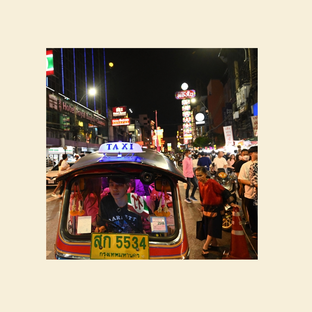 A photo of a tuktuk on a busy street at night.